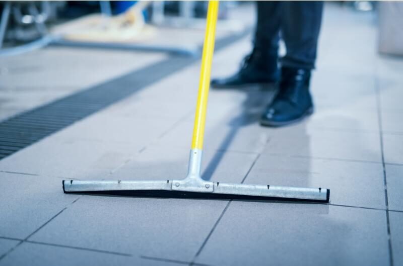 Close-up of a floor wiper mop being used on tiled flooring in an industrial setting.